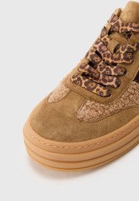 Tan suede sneaker with textured beige accents and a leopard print lace. Features a thick tan rubber sole with layered ridges.