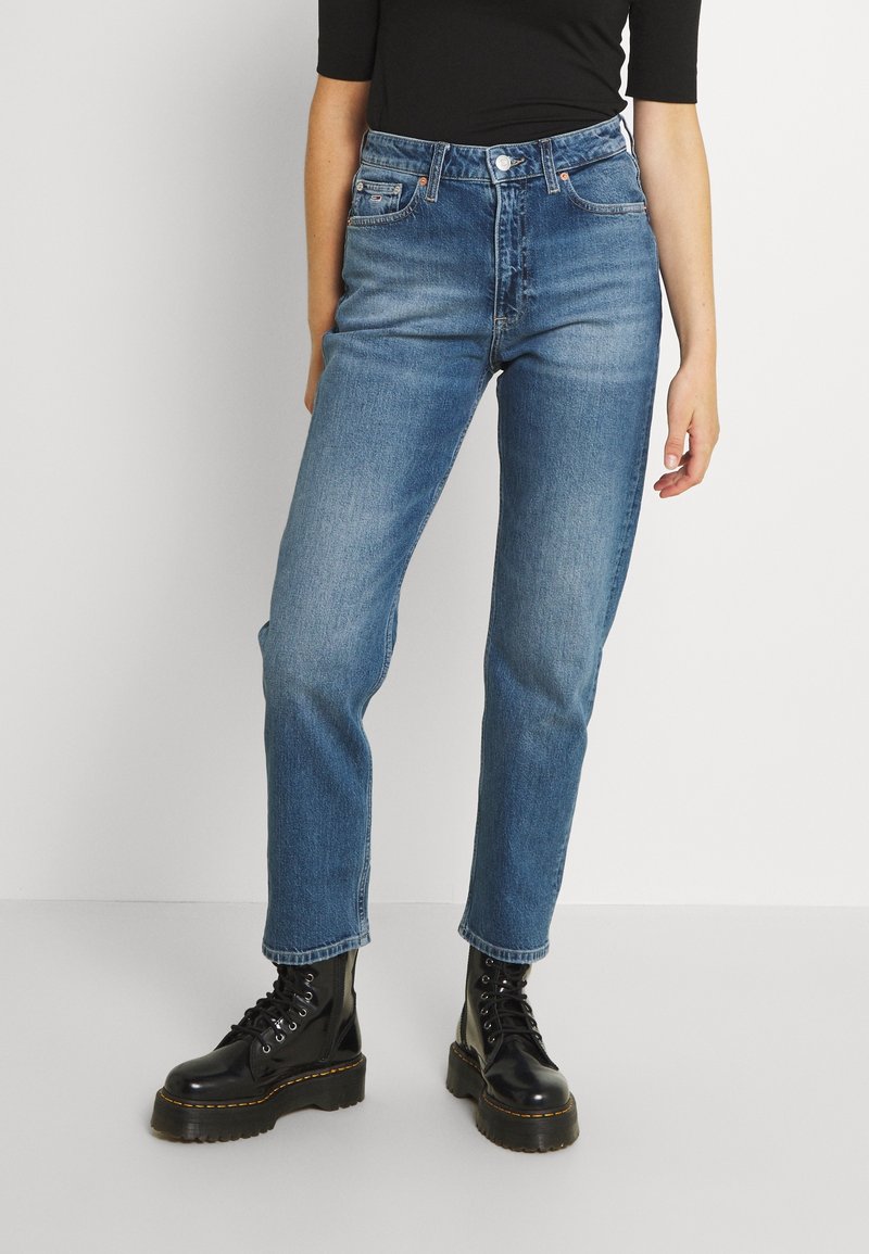 Person wearing high-waisted blue jeans and black platform lace-up boots, standing against a plain white background.