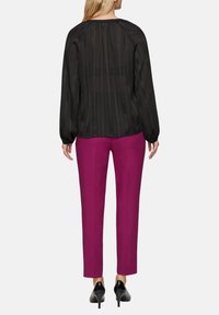 Blouse noire et transparente à manches longues et rayures verticales, associée à un pantalon ajusté de couleur magenta vif et des escarpins noirs.
