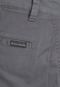 Pantalon en denim gris avec une texture subtile, doté d'une poche arrière avec une étiquette noire "TOM TAILOR" et des coutures contrastantes.