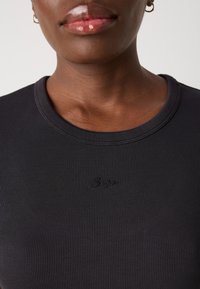 Black ribbed short-sleeve top featuring a round neckline and subtle embroidered logo centered on the chest. Smooth, textured fabric.