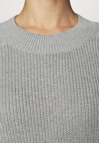 Šedý pletený svetr s vroubkovaným kulatým výstřihem, texturovanou látkou a jemným vzhledem, zdůrazňující tkané vzory.