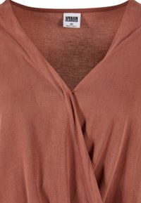 Top enveloppant couleur rouille en tissu doux, avec un décolleté en V et des fronces au centre, présentant une texture lisse et un design léger.