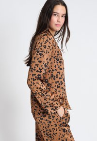 Brązowa bluzka w łaty w leopardzie z długimi rękawami i luźnym fasonem. Miękka tkanina, lekki połysk i okrągły dekolt.