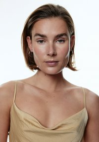 Lichtbeige satijnen top met een kraagontwerp en dunne spaghettibandjes. Gladde textuur en een getailleerd silhouet. Minimalistische stijl.