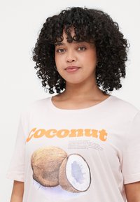 Light pink cotton t-shirt featuring a coconut graphic and orange text. Round neckline, short sleeves, soft texture, and relaxed fit.