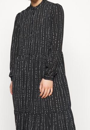 Robe noire avec un devant à boutons, un col rond, des manches longues et des rayures verticales blanches, avec une section de jupe en tiers.