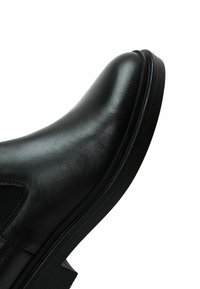 Botte Chelsea en cuir noir avec bout arrondi, panneau latéral élastique et petit talon empilé.