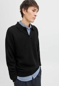 Sort, tekstureret striktrøje med en flettet krave, båret over en blå og hvid stribet skjorte. Slim fit, ribbet kant og manchetter.