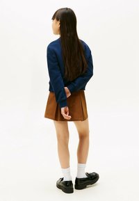 Felpa blu con polsini a coste, gonna pieghettata marrone e scarpe con plateau nere, abbinate a calzini bianchi, viste da dietro.
