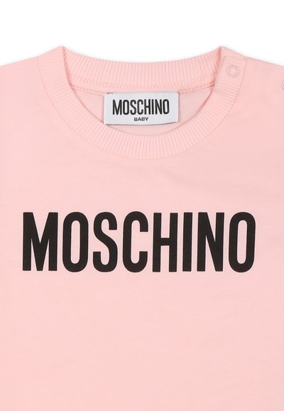 Maglietta per bambino rosa con scollatura a girocollo a costine e testo nero "MOSCHINO" al centro. Include chiusure a scatto sulla spalla.