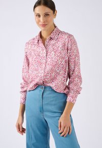 Camisa de manga larga con botones en tela rosa con un patrón floral. Cuenta con cuello y un corte relajado, combinada con vaqueros azules de talle alto.