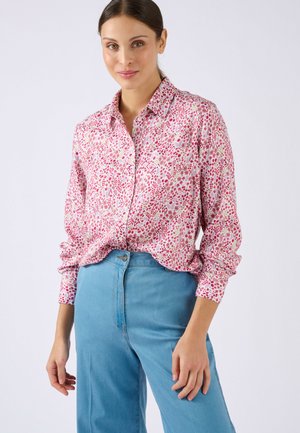 Camicia a maniche lunghe con bottoni in tessuto rosa con motivo floreale. Presenta un colletto e una vestibilità morbida, abbinata a jeans blu a vita alta.