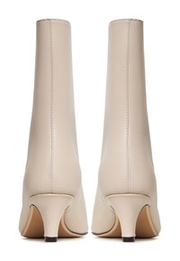 Paire de bottines en cuir beige avec talons courts effilés, vues de dos sur fond blanc.