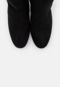 Botas de tobillo de ante negro con una textura suave, punta redondeada y detalles de costura mínimos. Sin hardware visible ni patrones.