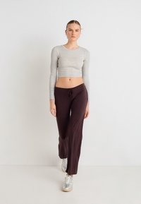 Hall helelõikega pika varrukaga pluus, millel on tumedat pruunid laiade jalgadega püksid, millel on paelaga vöökoht, kantud hõbedaste spordijalatsitega.