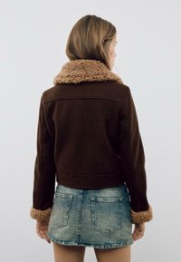 Brun cropped jakke med et tekstureret, faux fur-krave og manchetter. Sættes sammen med en denim mini-sukne med et klassisk fem-lommers design.