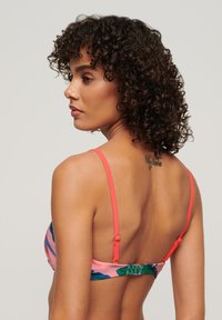 Top bikini con motivo floreale rosa e verde, sottili spalline corallo, chiusura regolabile sul retro e texture delicata.