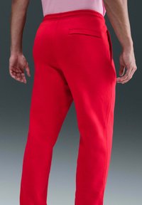 Rode joggingbroek met een slanke pasvorm, elastische tailleband en een achterzak. De stof lijkt zacht met een gladde textuur.