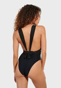 Crni jednodijelni kupaći kostim sa širokim naramenicama, niskim leđima i detaljem vezanja u struku. Glatka tekstura s prilagođenim dizajnom.