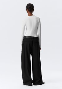 Witte lange mouwen top en zwarte wijde broek met een gladde textuur. De broek heeft een soepele afwerking en een zwarte riem met twee achterzakken.