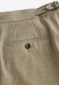 Pantaloni bej cu dungi, având un design adaptat, dotati cu un buzunar posterior închis cu un nasture maro și dungi fine verticale albe.