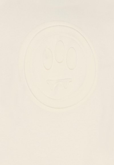 Kremowa tkanina zdobi teksturowane, okrągłe logo z twarzą, w tym trzema owalnymi oczami i dwoma spiczastymi zębami na dole.