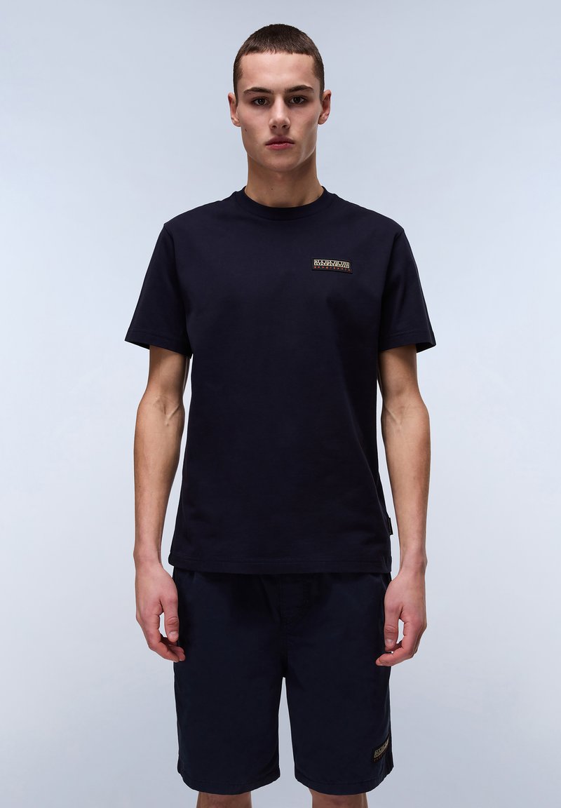 Marineblå bomulds T-shirt med korte ærmer og et lille logo patch på brystet, parret med marineblå shorts med detaljer på siden.