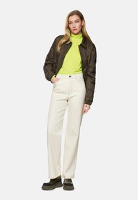 Brown quilted bomber jacket, neon green turtleneck, cream wide-leg jeans with studs on the pocket, and black chunky sole boots.