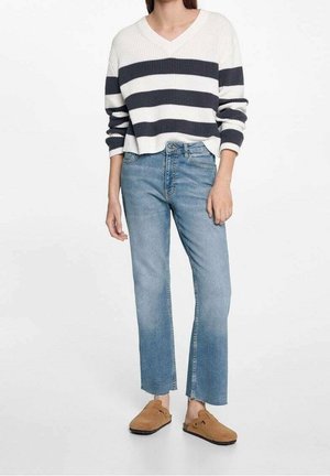 V-kaulaus valkoisin ja laivastonsinisin raidoituksin varustettu villapaita, yhdistettyinä vaaleansiniset suorat farkut ja ruskeat liukuhihnakengät. Taitava neulemateriaali.