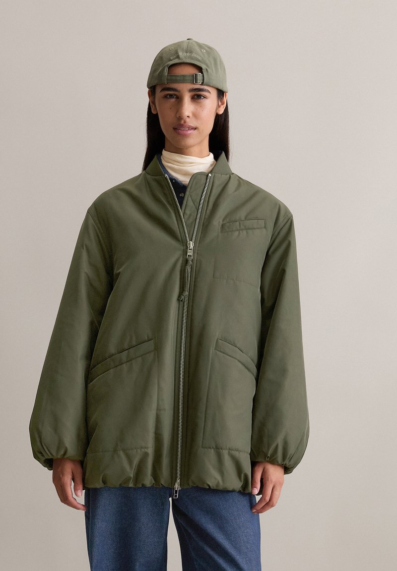 Groene nylon jas met een rits aan de voorkant, twee zijzakken en een gekorte zoom. Vergezeld van een bijpassende pet met een eenvoudig ontwerp.