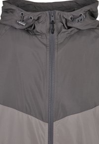 Mörkgrå huva jacka med frontdragkedja och justerbara dragsko i huvan, visad från bröstet och uppåt.