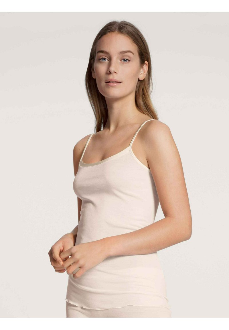 Top in crema con spalline sottili, realizzato in un tessuto morbido e elasticizzato. Presenta un collo a barchetta e bordi senza cuciture per il massimo comfort.