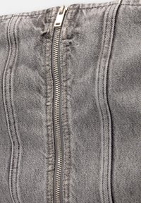 Grijze denim stof met een centrale metalen rits. De textuur is licht versleten met zichtbare stiksels en subtiele variaties in tint.