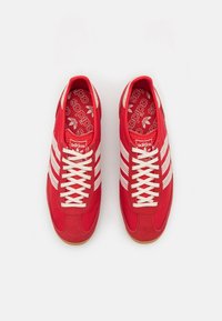 Röda canvas-sneakers med vita ränder, med en texturerad tånosa, tjocka snören och en mönstrad innersula. Gummisula med gummifinish.