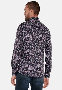 Langärmliges Hemd aus schwarzem Stoff mit buntem Blumenmuster, Button-Down-Kragen und einer taillierten Passform, die von hinten sichtbar ist.