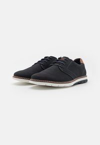 Chaussures noires en mesh avec un embout rond et un accent de talon marron contrastant. Présente un dessus texturé, une semelle intermédiaire blanche et une semelle extérieure en caoutchouc texturé.