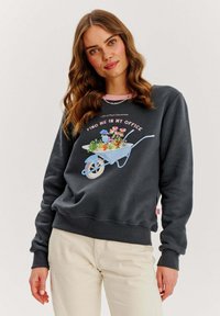 Tmavošedá mikina s grafickým motívom modrého fúrika plného kvetov. Má ružový akcent na výstrihu a rebrované manžety.