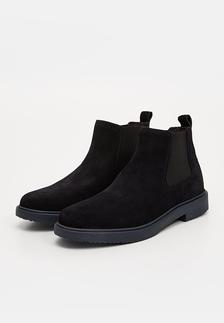 Bottines noires en suede avec des panneaux élastiques sur les côtés et une semelle en caoutchouc texturé. Présentent une finition lisse et un design minimaliste.