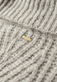 Gray knitted fabric featuring ribbed texture. A small gold metal tag labeled "Giuferdy" is embedded in the knit.