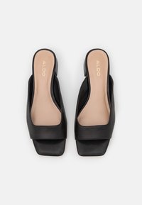 Sandales en cuir noir à semelle plate avec un bout carré et un dos ouvert. Semelle intérieure beige clair avec logo de la marque en relief. Texture lisse et design minimaliste.