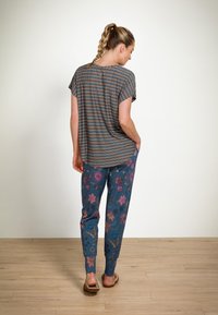 Gestreepte kortemouwtop in het blauw, gecombineerd met bloemenpatroonblauwe broek met roze en paarse accenten. Het model draagt bruine sandalen.