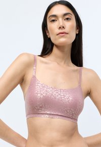 Lyserød bralette med tynde stropper, der har et subtilt metallic leopardmønster. Glat tekstur, bredt bånd under og et blødt, tætsiddende design.