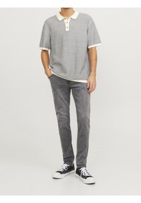 Camisa polo a rayas grises y blancas con tres botones, combinada con jeans ajustados grises y zapatillas negras con cordones blancos.