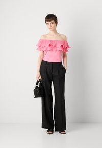 Top rosa sin hombros con volantes, combinado con pantalones de pierna ancha negros. El modelo sostiene un pequeño bolso negro.