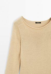 Maglione beige lavorato a maglia con maniche lunghe e scollatura rotonda, che mostra una texture a maglia dettagliata e una piccola etichetta nera all'interno del colletto.