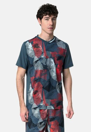 Giovane uomo con maglietta sportiva a maniche corte e pantaloncini abbinati con motivi astratti rossi, bianchi, neri e grigi.