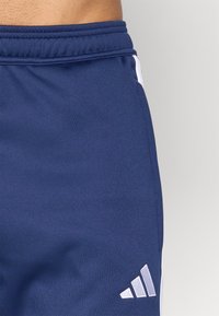 Marineblauwe sportshorts van gladde stof, met een witte streep aan de zijkant en een kenmerkend wit merklogo aan de onderzijde links.