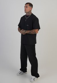 Fekete pamut póló rövid ujjakkal, kis logóval, fekete széles szárú nadrággal és szürke sportcipővel, fehér részletekkel párosítva.