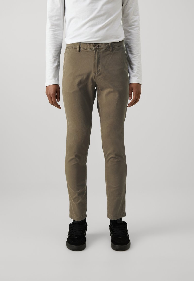 Khaki chinos with a slim fit, made of smooth cotton fabric. Features a button closure and belt loops. Worn with black sneakers.
